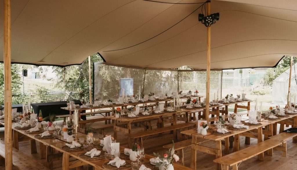 Stilvoll dekoriertes Stretchzelt in Holzoptik mit langen Holztischen und rustikaler Hochzeitsdekoration von Mo’s Tent & Event