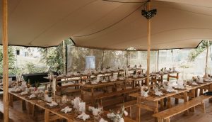 Stilvoll dekoriertes Stretchzelt in Holzoptik mit langen Holztischen und rustikaler Hochzeitsdekoration von Mo’s Tent & Event