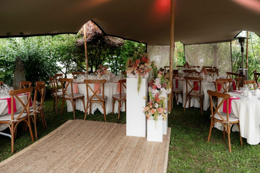 Elegantes Hochzeitszelt mit gedeckten Tischen, Holzstühlen und floraler Dekoration im Grünen